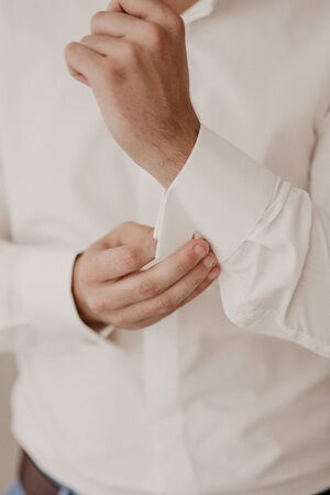 Hands button up the buttons on his shirt. The process of fastening the buttons on his white shirt....