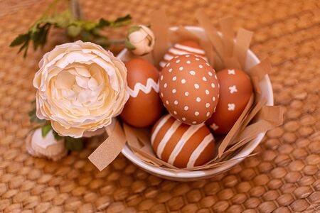 Painted brown eggs with various white patterns for Easter holiday on plate. Natural Homemade Colored...