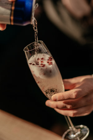 Happy Valentines day celebration concept. Man pouring sparkling champagne in glass with red heart shaped confetti. Love potion in glass. Close upの写真素材