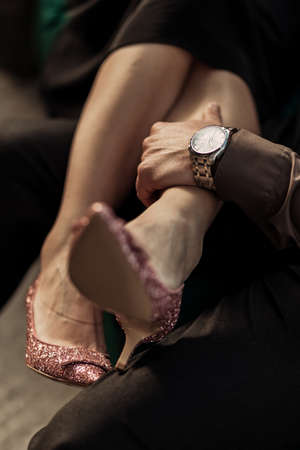 Close up a woman putting her legs in rose golden high heels on man. Man holding womans feets on his knees. Elegant couple sitting on sofa. Valentines love dayの写真素材