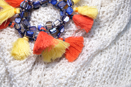 Colorful Fashion bracelets decorated with tassels on white soft wool scarf close-up image.