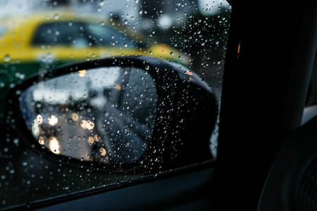Side mirror and rain drops at the cars window while driving on the road, in the evening.の写真素材