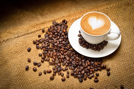 A cup of coffee with latte art of heart and coffee bean on a testure background