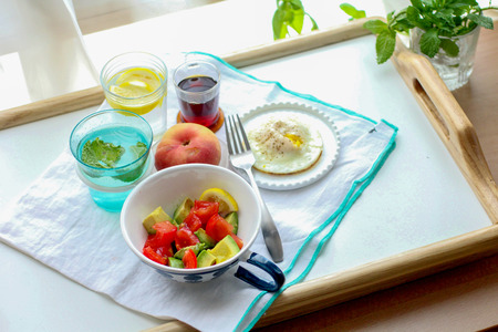 dietary meal with avocado and tomato salad, fry egg, apple and juice on a wooden trayの写真素材