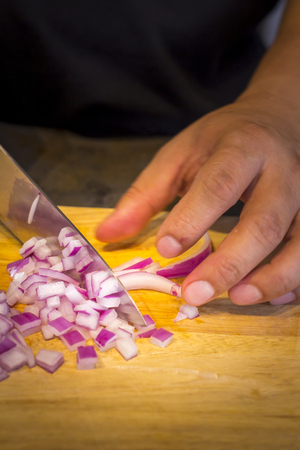 Chef chopping a red onion with a knife on the cutting board.