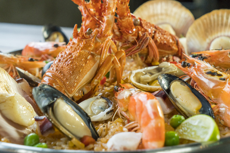 Gourmet seafood Valencia paella with fresh langoustine, clams, mussels and squid on savory saffron rice with prawn, scollops, mussels and lime slices, close up viewの写真素材