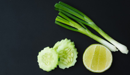 Green vegetables, onions, sliced lime and cucumbers, on black chalkboard. top view, space for textの写真素材