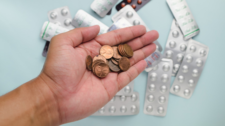 Stack of US dollar coin in man's hand with blur drug pack as background refer to cost of health careの写真素材