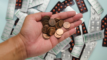 Stack of US dollar coin in man's hand with blur drug pack as background refer to cost of health careの写真素材