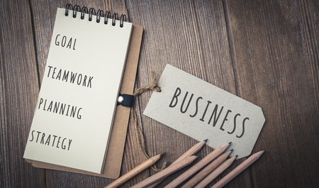 list of a business plan notebook place on a wooden table with pencils.の写真素材