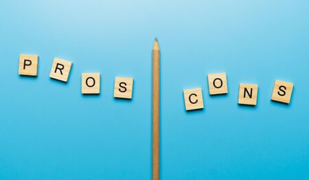 "Pros and Cons" word in the wooden block on blue background separated by a pencilの写真素材