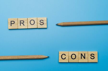 "Pros and Cons" word in the wooden block on blue background pointed by pencilの写真素材