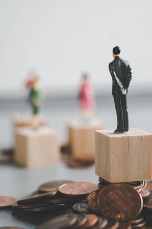 Gender gap, difference income between man and woman, miniature man and woman stand on coin stacksの写真素材
