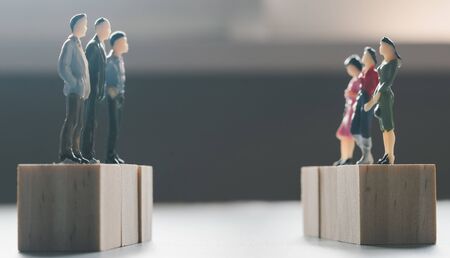 Miniature men and women stand on wooden cube confront each otherの写真素材