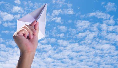 throwing paper plane to the sky, human's hand holding paper craft against blue sky backgroundの写真素材