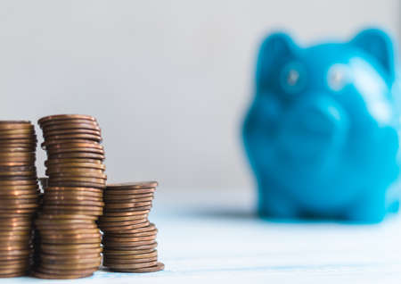 close up coin stacks and blurry piggy bank on white tableの写真素材