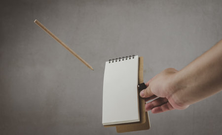 Photo of a floating object. Human hand holding a notebook with a pen that floats in the airの写真素材