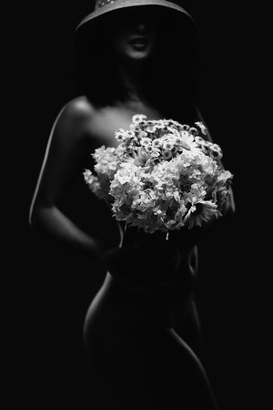 Naked young seductive woman with flowers in hand. Select focus on flowersの写真素材