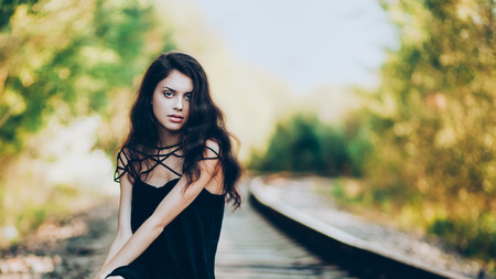 Artistic fashion portrait of young brunette sitting on railroad. Shallow depth of fieldの写真素材