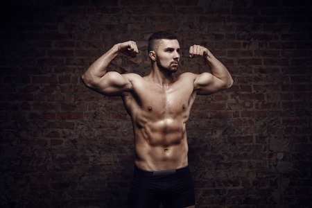 Young muscular man showing double biceps near red brick wallの写真素材