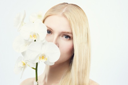 Young gorgeous blond with orchid on white, hiding her lips with flowerの写真素材