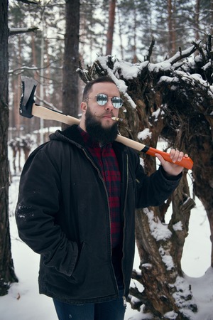 Bearded man with axe in winter outdoors, smocking cigar. Shallow depth of fieldの写真素材