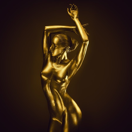 Golden naked feminine woman like statue posing on dark backgroundの写真素材