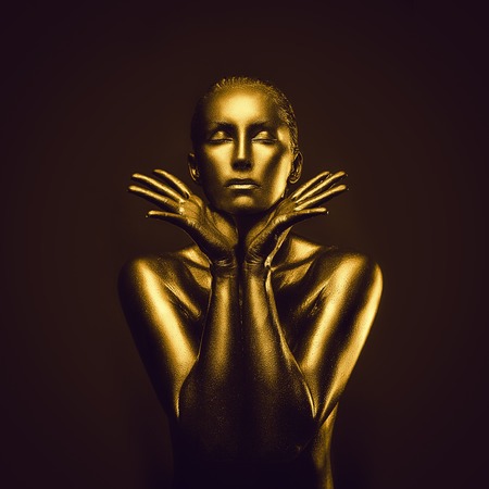 Golden naked feminine woman like statue posing on dark backgroundの写真素材