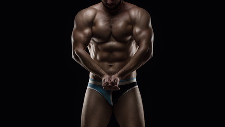 Young muscular man posing on black background