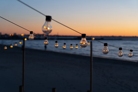 Close up of the glowing light bulbs at the beach cafe terrace. Sun is setting in the blurry abstract background.の写真素材