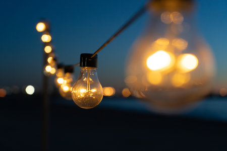 Close up of the glowing light bulbs at the beach cafe terrace. Sun is setting in the blurry abstract...