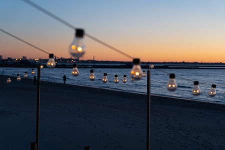 Close up of the glowing light bulbs at the beach cafe terrace. Sun is setting in the blurry abstract background.の写真素材