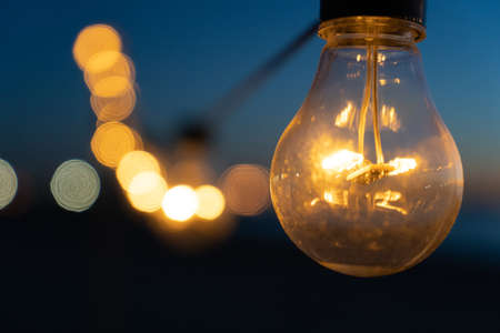 Close up of the glowing light bulbs at the beach cafe terrace. Sun is setting in the blurry abstract background.の写真素材