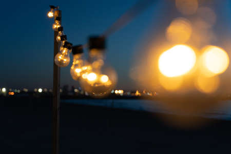 Close up of the glowing light bulbs at the beach cafe terrace. Sun is setting in the blurry abstract background.の写真素材