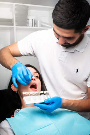 The patient at the dentist looks at his teeth through the mirror, selects the color of the teeth from the teeth paletteの写真素材