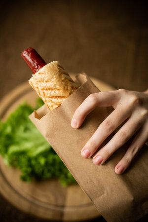 feemale hand holding French hot dog on a wood background, fast food and copy space. close-upの写真素材