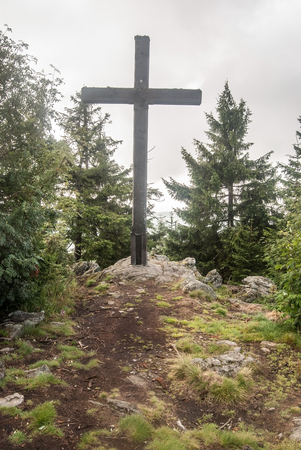 wooden cross on Sibensteinkopf hill summit with trees around and cloudy sky in Bavarian Forest mountains in Germanyの写真素材