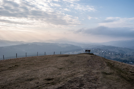 Ochodzita hill with meadow, bench and hills on the background above Koniakow village in Beskid Slaski mountains in Poland during late autumn day with blue sky and cloudsの写真素材