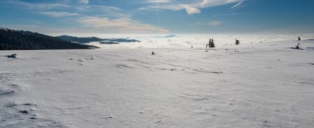 snow covered mountain meadow with hills on the background and blue sky with clouds - winter on...