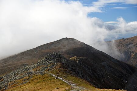 Derese hill in Nizke Tatry mountains in Slovakia with few rocks and hiking trail during autumn day with blue sky and cloudsの写真素材