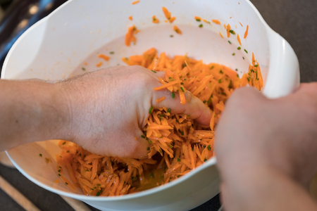 Carrot salad preparation with hand in white bowlの写真素材