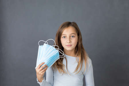 Portrait of a young girl with fan made of medical masks in her hand on grey background.の写真素材