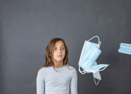 Portrait of a young scared girl watching flying medical masks on grey background.の写真素材