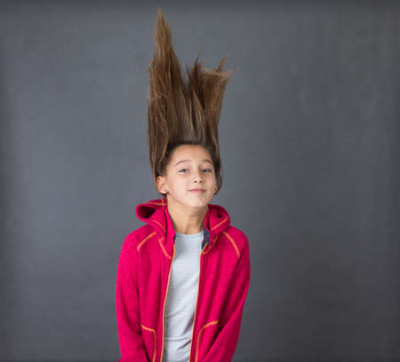 Portrait of a young funny happy girl in red sweater with her hair up in the air on grey background with space for textの写真素材