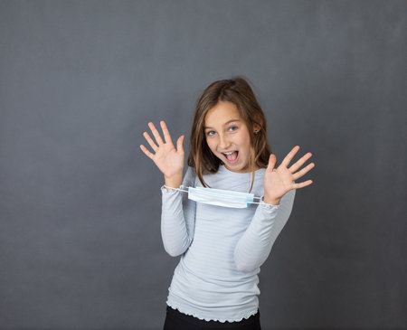 Portrait of young smiling girl giving up with medical mask on her hands on grey background.の写真素材