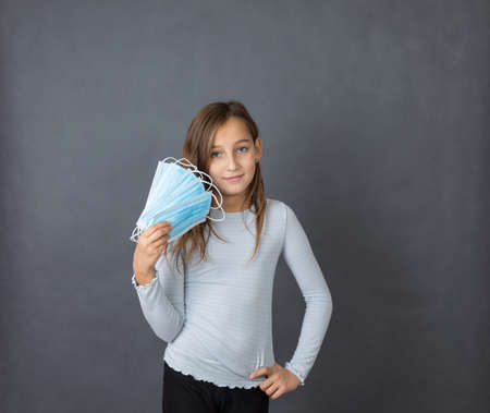 Portrait of a young girl with fan made of medical masks in her hand on grey background.の写真素材