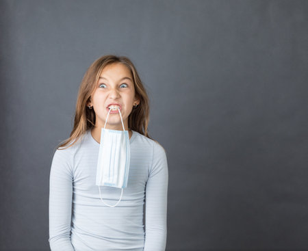Portrait of a young angry girl with medical mask in her mouth on grey background.の写真素材