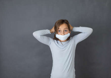 Portrait of a young girl puttin on medical mask on grey background.の写真素材