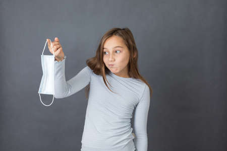 Portrait of a young up sad girl with medical mask on her finger on grey background.の写真素材