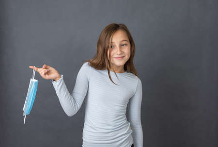 Portrait of a young happy girl playing with medical mask on grey background.の写真素材